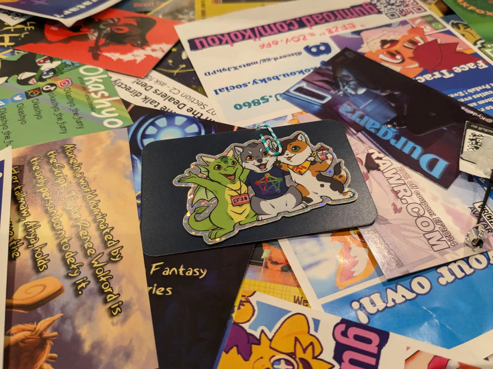 Photo of a table with a huge pile of business cards, and our Fediverse stickers on top, attached to a blue business card