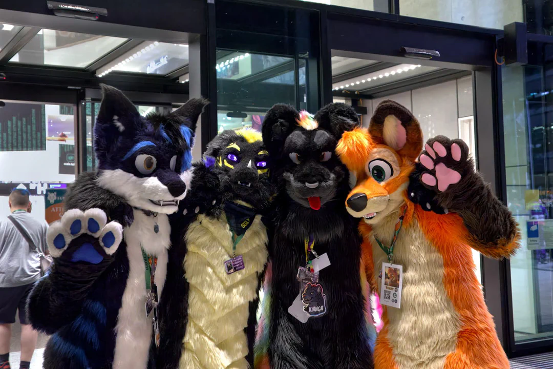 Photo of an arctic fox, dragon, black jaguar, and red fox fursuiter, standing in front of the entrance to the CCH lobby