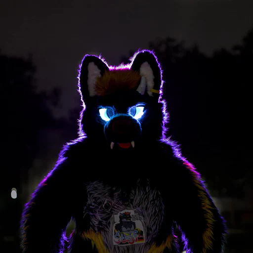 Close-up photo of a dragon-wolf fursuiter with glowing blue eyes, looking directly at the camera. He is lit with purple backlight.