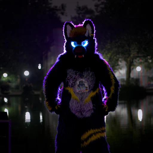 Photo of a dragon-wolf fursuiter with glowing blue eyes, looking directly at the camera with his hands on his hips. He is lit with purple backlight.