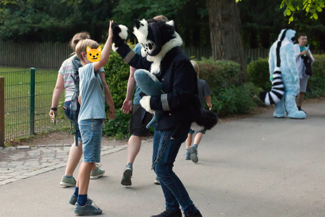 A black and white demon dog fursuiter giving high fives to a group of kids