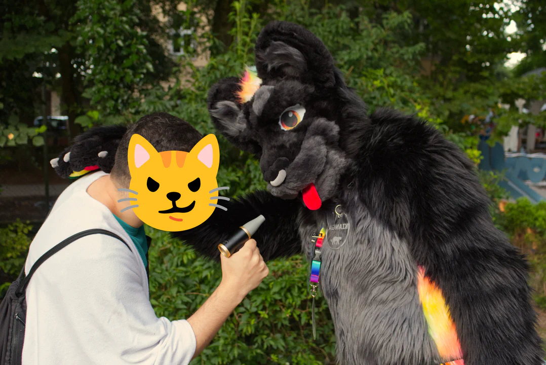 A black jaguar fursuiter getting some cool air from a non-suiter friend, who is holding a fan to his muzzle