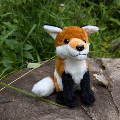 Photo of a small red fox plush, now sitting on a tree stump with dense grasses and vegetation in the background