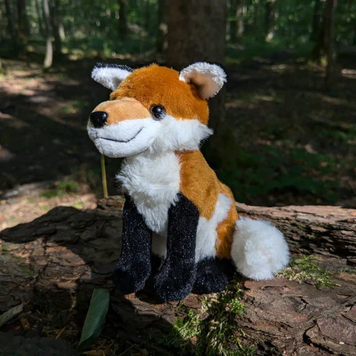 Photo of a red fox plush sitting on a tree stump in the woods.