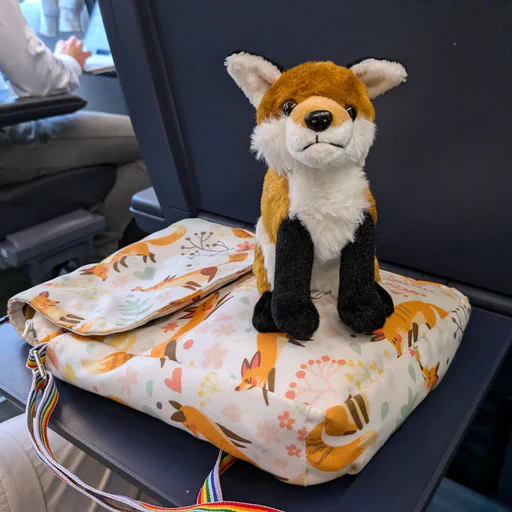 Photo of a little red fox plush sitting on a train seat table
